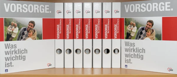 Das Foto zeigt eine Reihe von Aktenordnern, die nebeneinander aufgestellt sind. Die Ordner haben eine weiße untere Hälfte mit der Aufschrift „Was wirklich wichtig ist“ und eine rote obere Hälfte mit der Aufschrift „VORSORGE. Was wirklich wichtig ist.“ Zudem sind auf den Rücken der Ordner Bilder von glücklichen, lächelnden Menschen in einer natürlichen Umgebung zu sehen.